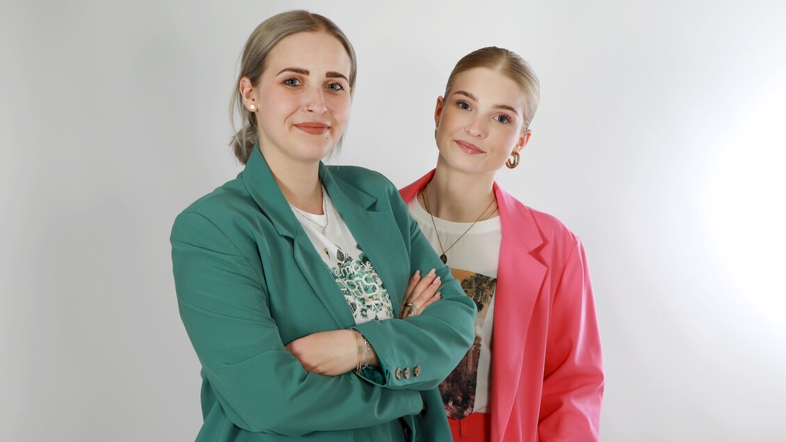 Zwei Frauen stehen nebeneinander und lächeln in die Kamera. Die Frau links trägt einen grünen Blazer, die rechts einen pinken Blazer. | © Franzis Spielzeugeck