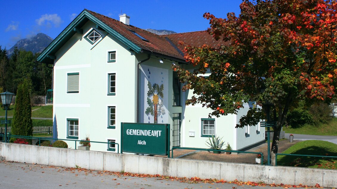 Ein schön gestaltetes Gemeindehaus mit einem bunten Wandgemälde. Im Hintergrund sind Bäume und Berge zu sehen. | © Gemeinde Aich