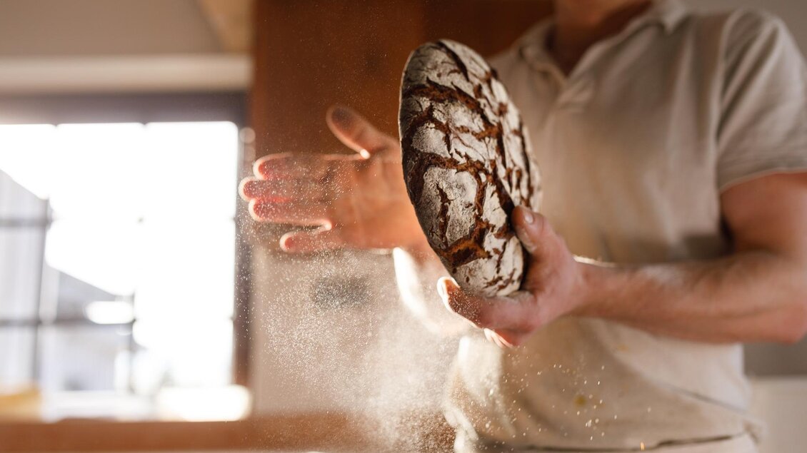 Ein Bäcker hält ein frisches Brot in der Hand. Mehlstaub schwebt in der Luft. | © Pixabay Intuitivmedia
