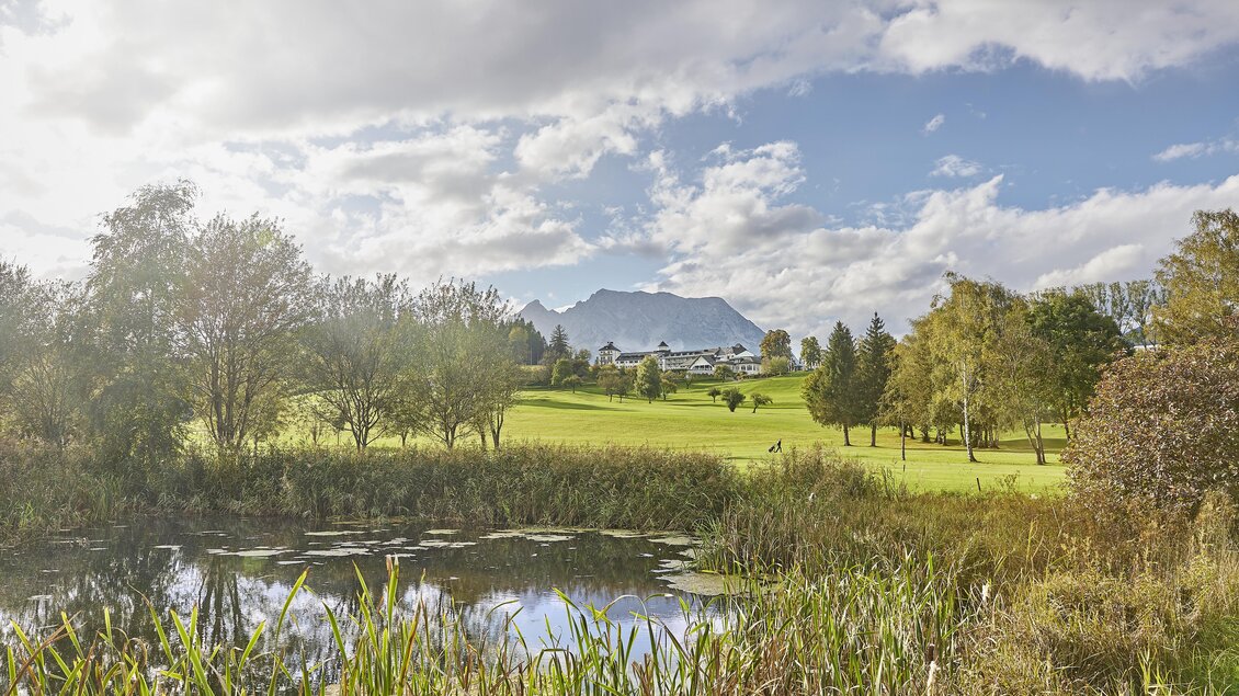 Eine malerische Landschaft mit einem Teich und grünen Wiesen. Im Hintergrund sind Berge und ein bewölkter Himmel zu sehen. | © Thomas Sattler