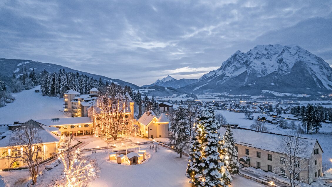 Eine winterliche Landschaft mit schneebedeckten Bäumen und zwei Gebäuden. Im Hintergrund sind majestätische Berge und ein bewölkter Himmel zu sehen. | © Thomas Sattler