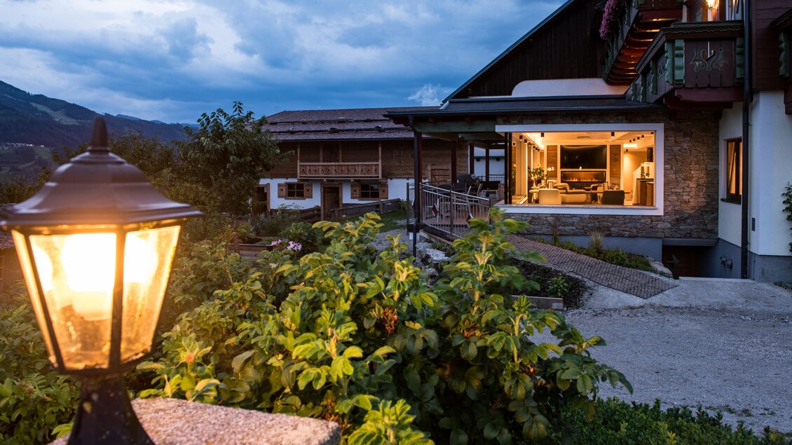 Ein charmantes Haus mit einem einladenden Außenbereich und einer warmen Lichtquelle. Die Umgebung ist grün und bietet einen Blick auf die Berge im Hintergrund. | © Shooting Star