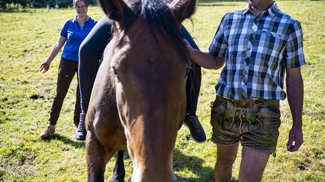 Ein Mädchen reitet auf einem Pferd, während ein Mann sie führt. Im Hintergrund steht eine weitere Person und die Umgebung ist ländlich. | © Karl Brandner