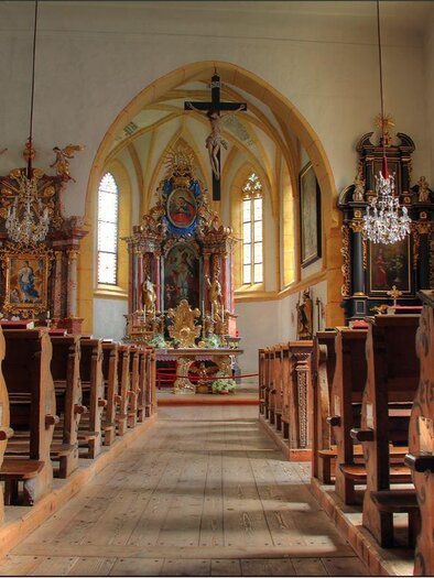 Ein schöner Innenraum einer Kirche mit hölzernen Bänken und kunstvollen Altären. Das Licht fällt durch große Fenster und beleuchtet den Raum. | © Katholische Kirche