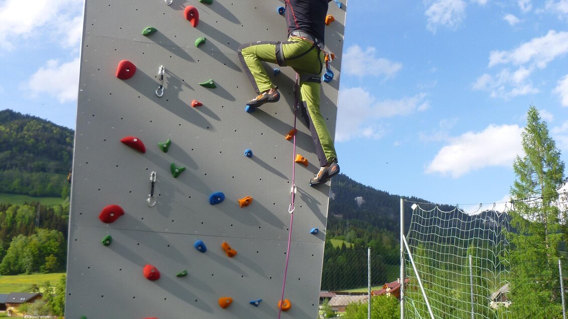 Eine Kletterwand im Freien mit einer Person, die das Besteigen übt. Im Hintergrund sind Bäume und ein blauer Himmel sichtbar. | © Gemeinde Aich