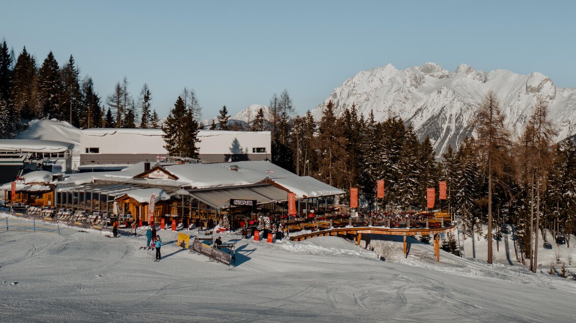 Ein Skigebiet mit einem gemütlichen Restaurant und vielen Sitzplätzen im Freien. Im Hintergrund sind schneebedeckte Berge und ein klarer Himmel zu sehen. | © Knapplhütte
