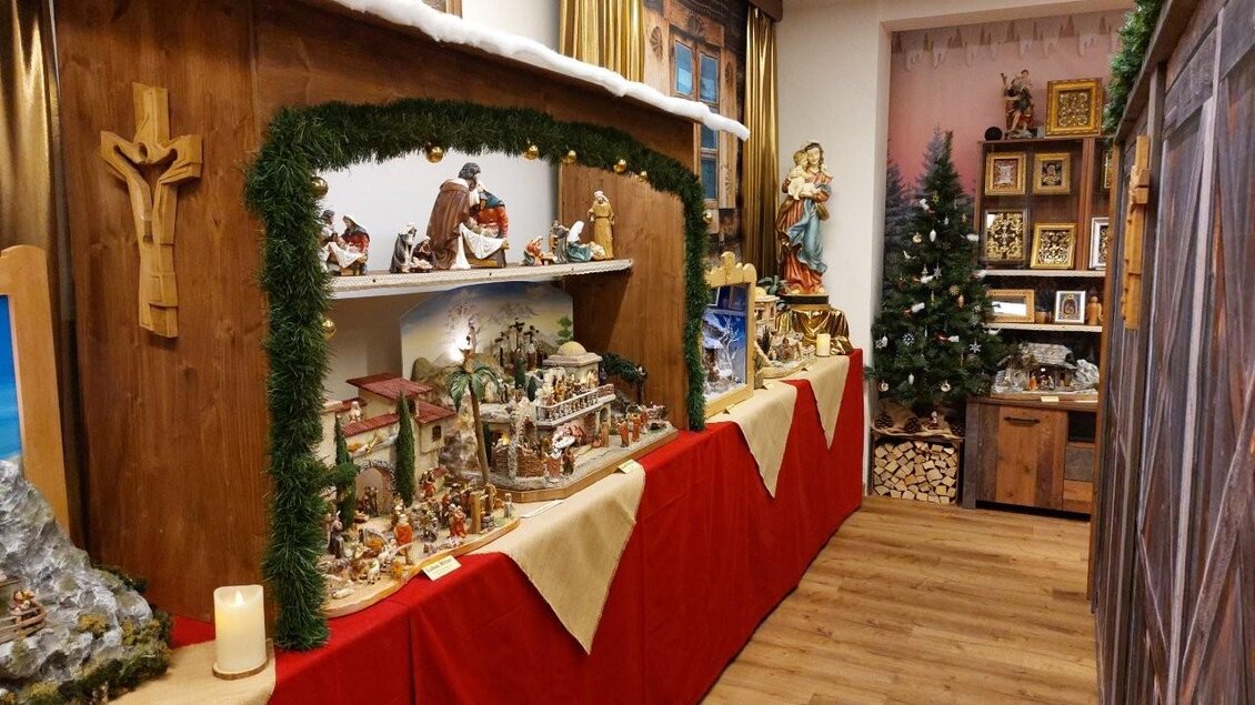 Eine festliche Weihnachtsausstellung mit kunstvoll gestalteten Krippen auf einem roten Tuch. Im Hintergrund sind ein Weihnachtsbaum und weitere Dekorationen zu sehen. | © Gerald Gerhardter