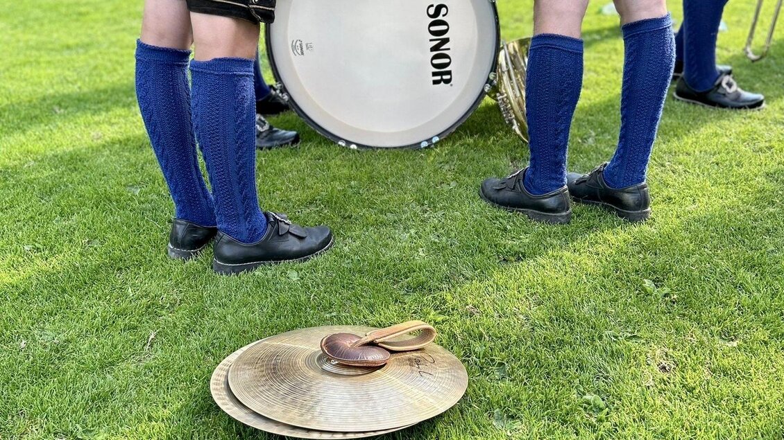 Eine Gruppe von Musikern in traditioneller Tracht steht auf einer grünen Wiese. Vor ihnen liegt ein Becken auf dem Boden, während ein großes Schlagzeug im Hintergrund steht. | © Marie Schwarzkogler-Krammer