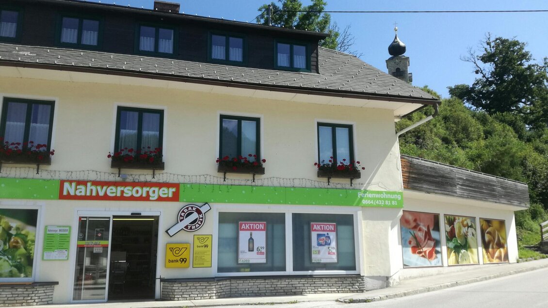 Ein kleiner Nahversorger in einem ländlichen Gebiet. Das Gebäude hat mehrere Fenster und eine angebaute Verkaufsfläche mit bunten Plakaten. | © Fam. Moser