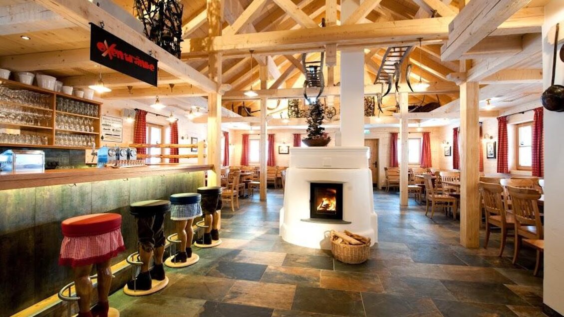 Ein einladendes Restaurant mit Holzdekor und gemütlicher Atmosphäre. Die Bar bietet bunte Hocker und einen offenen Kamin, der Wärme verbreitet. | © Oxenalm