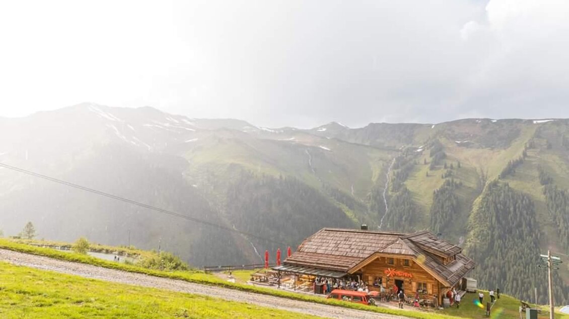 Eine Berghütte in einer grünen Landschaft mit beeindruckenden Bergen im Hintergrund. Der Himmel ist bewölkt und die Umgebung wirkt ruhig und einladend. | © Oxenalm