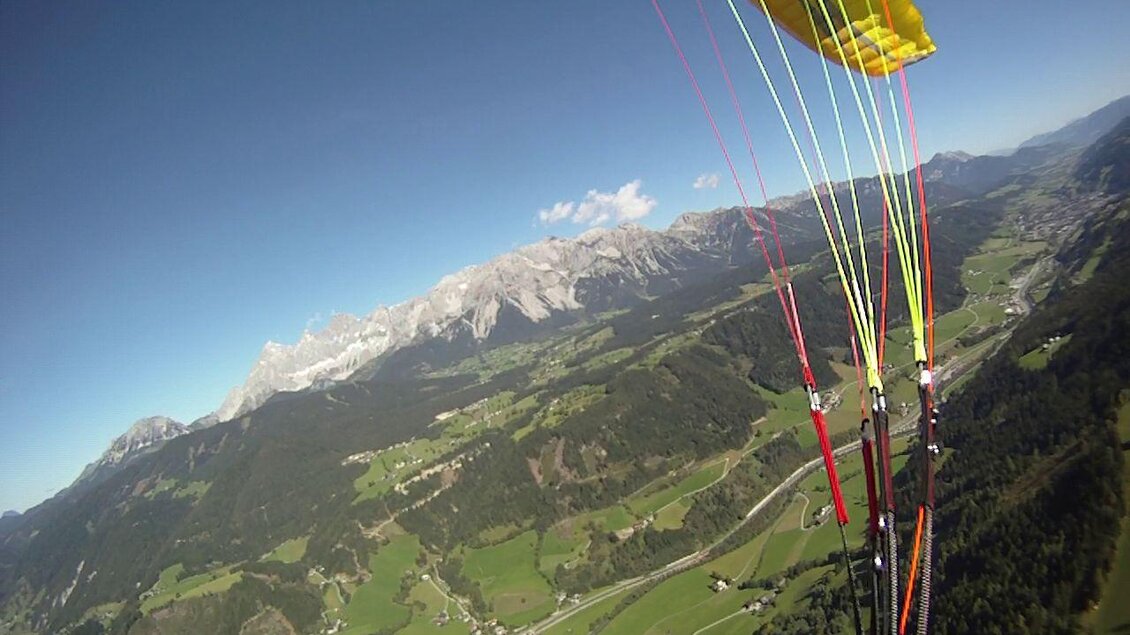Ein atemberaubender Blick auf grüne Täler und majestätische Berge aus der Luft. Der Gelbe Gleitschirm schwebt über der malerischen Landschaft. | © Flugschule Aufwind 