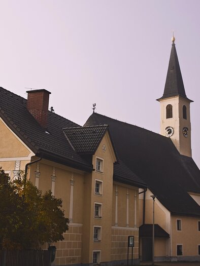 An old, yellow building with a tall church tower stands in the fog. The architecture appears traditional and quaint. | © Armin Walcher
