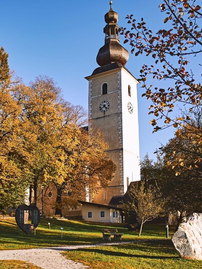 A beautiful place with a tall tower and colorful autumn trees. The sky is clear and the scene feels peaceful. | © Armin Walcher