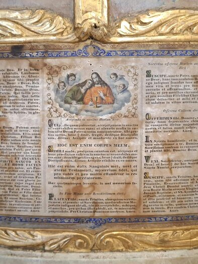 A decorative wall relief with golden embellishments and a central depiction. In the center, fragments of text can be seen, surrounded by elaborate ornaments. | © Beate Koller