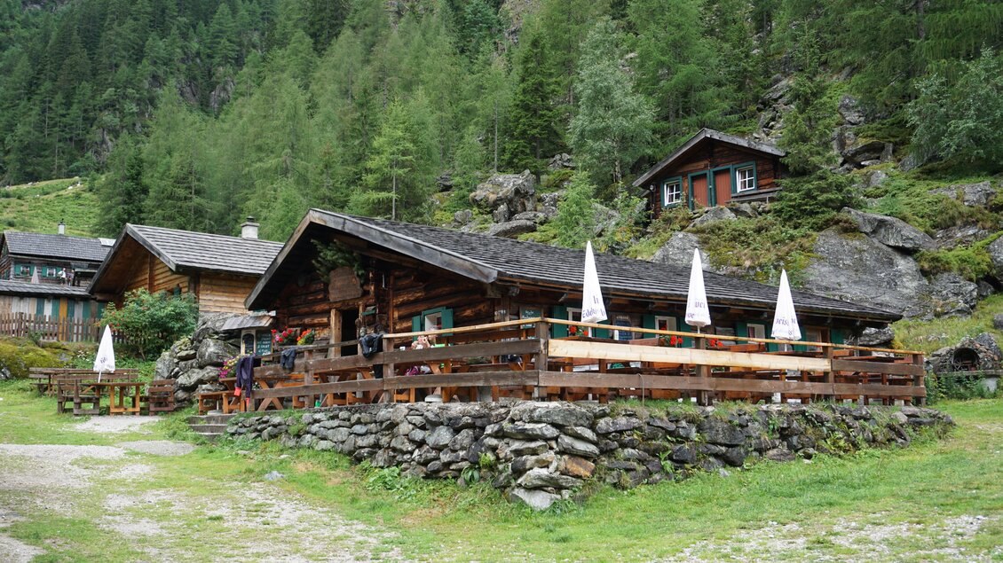 Eine gemütliche Almhütte umgeben von grünen Wäldern und Bergen. Die Terrasse ist mit Sonnenschirmen ausgestattet und lädt zum Verweilen ein. | © Naturpark Sölktäler