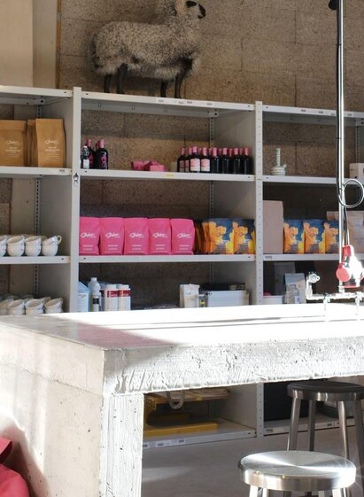 A modern room with shelves containing various products such as cosmetics and food. In the middle stands a large concrete table.