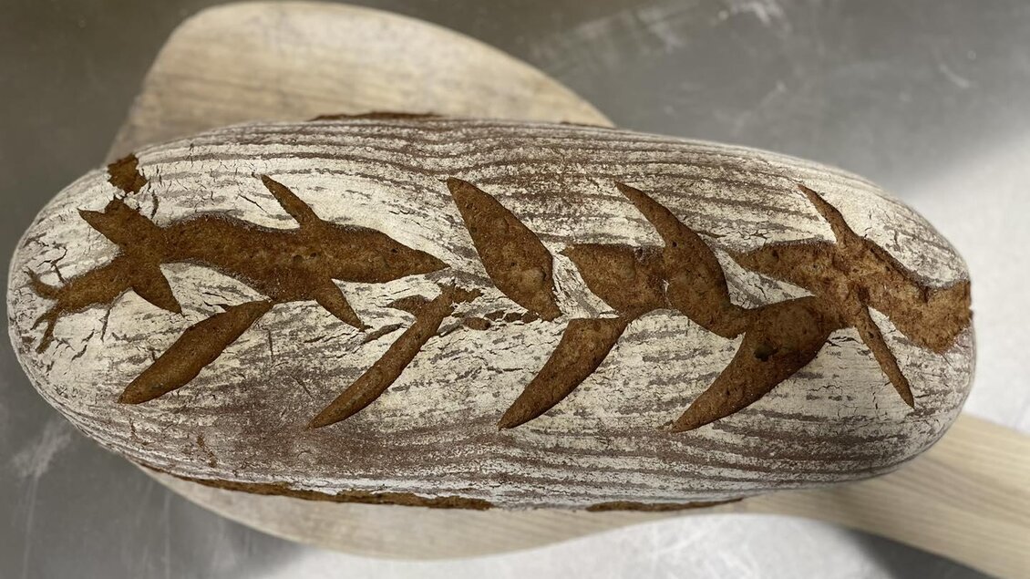 Ein frisch gebackenes Brot mit kunstvollen Mustern auf der Oberfläche. Die Dekoration zeigt stilisierte Blätter und Fische. | © Perner Alexandra