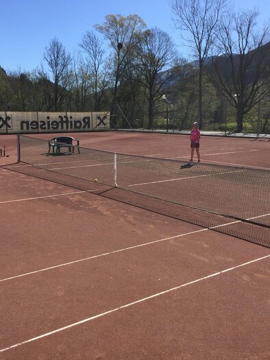 A tennis court with two players in athletic clothing. Trees and mountains are visible in the background. | © TC-Pichl