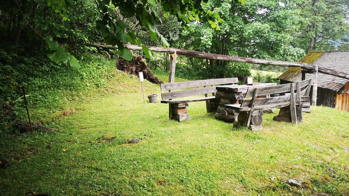 Ein ruhiger Garten mit einer hölzernen Bank und Tisch. Umgeben von grünen Bäumen und Rasen. | © Naturpark Sölktäler