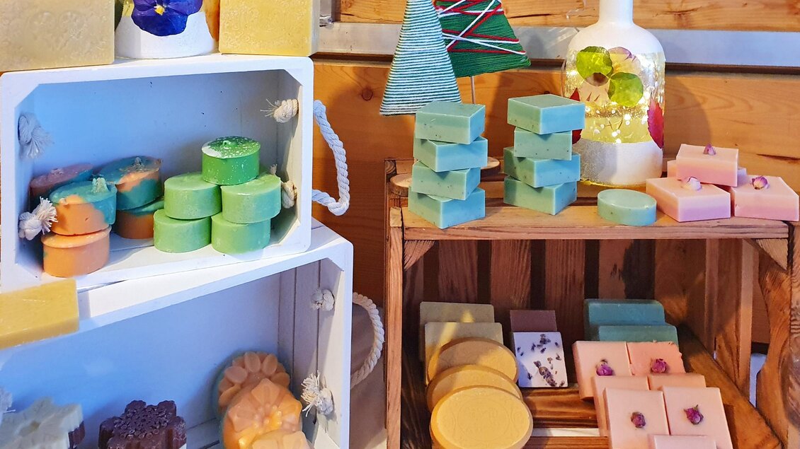 Ein schöner Marktstand mit bunten Seifen in verschiedenen Formen und Farben. Die Seifen sind ordentlich auf Regalen und in Körben angeordnet. | © Verena Novak