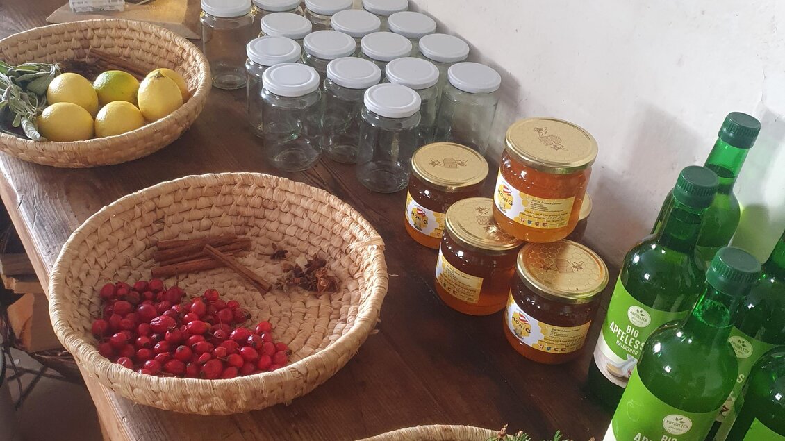 Ein Tisch mit verschiedenen Lebensmitteln und Zutaten. Es gibt Körbe mit frischen Kräutern, Zitronen und Beeren sowie Gläser und Flaschen mit Honig und Getränken. | © Verena Novak