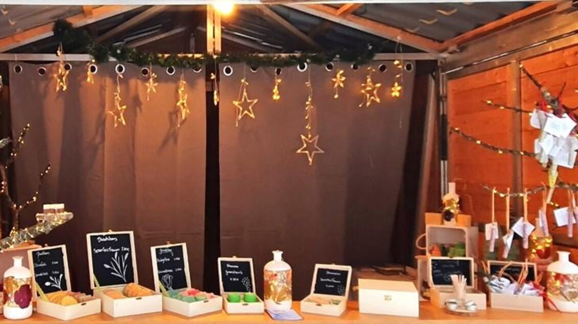 Ein gemütlicher Verkaufsstand mit Holzregalen, auf denen verschiedene Produkte präsentiert werden. Der Stand ist festlich dekoriert mit Lichtern und Sternen. | © Verena Novak