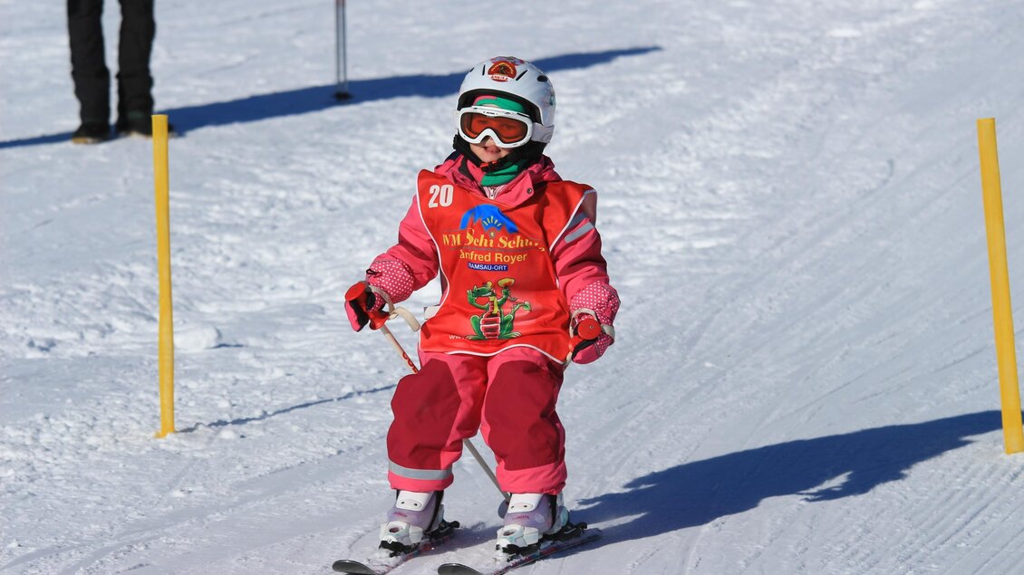 Ein kleines Kind in roter Skiausrüstung fährt auf einer Skipiste. Es trägt einen Helm und Sonnenbrille. | © WM-Schischule Royer