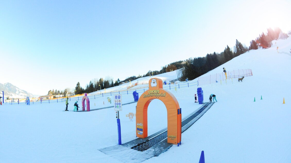 Ein schneebedeckter Hang mit einem bunten Kinder-Skigelände und einem Starttor. Im Hintergrund sind Freude beim Skifahren und die schöne Winterlandschaft zu sehen. | © Hauser Kaibling