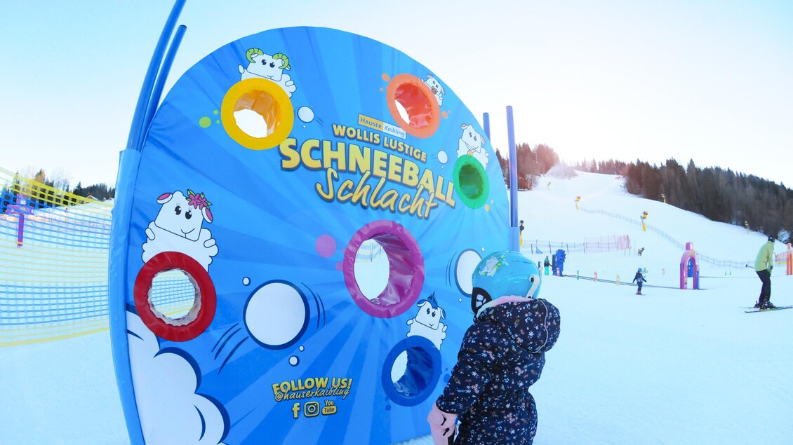 Ein farbenfrohes Spielbrett mit dem Thema "Schneeballschlacht" steht im Schnee. Im Hintergrund sind Skifahrer und eine Winterlandschaft zu sehen. | © Hauser Kaibling