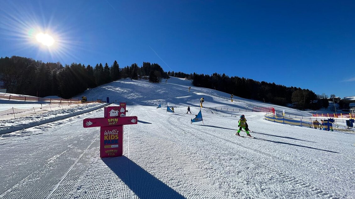 Eine sonnige Wintersportlandschaft mit schneebedeckten Pisten. Kinder und Erwachsene skifahren unter einem klaren blauen Himmel. | © Hauser Kaibling