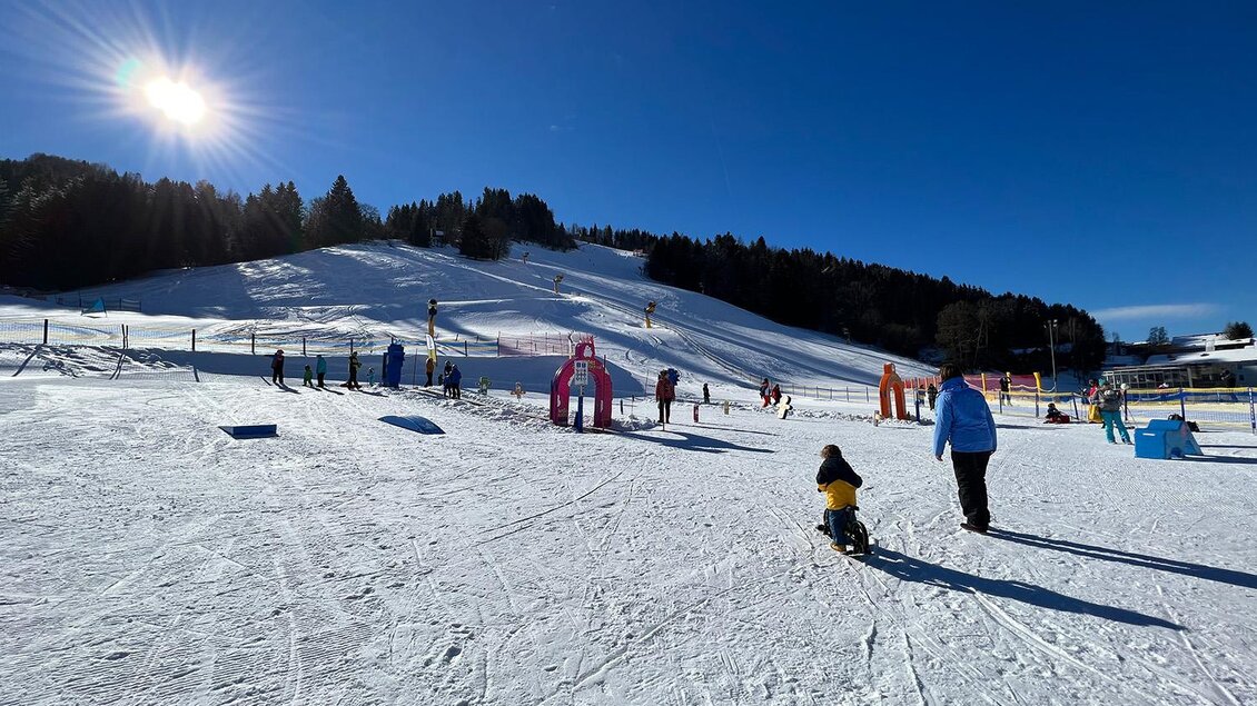 Ein sonniger Wintertag auf einem Skiübungsgelände. Kinder spielen im Schnee und genießen die klare, blaue Himmel. | © Hauser Kaibling