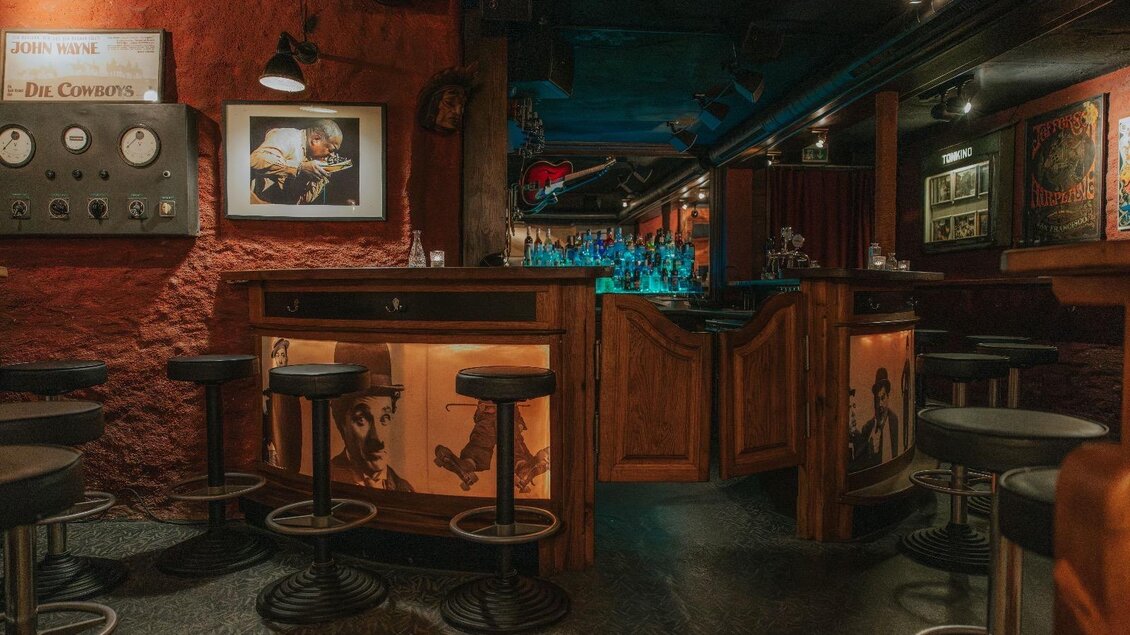Eine gemütliche Bar mit einem hölzernen Tresen und modernen Barhockern. Die Wände sind rot gestrichen und mit Kunstwerken dekoriert, während eine sanfte Beleuchtung eine entspannte Atmosphäre schafft. | © Daniela Pattermann