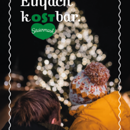 Ein Pärchen sitzt mit dem Rücken zur Kamera vor einem festlich beleuchteten Weihnachtsbaum. Die Lichter strahlen in warmen Farben und schaffen eine gemütliche Atmosphäre. | © Oststeiermark Tourismus
