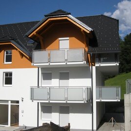 A modern building with orange accents and several balconies. Surrounded by green meadows and a clear blue sky.