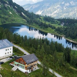 <p>Eine malerische Landschaft mit zwei Hütten am Ufer der Großsee. Umgeben von grünen Bergen und Bäumen, strahlt die Szene Ruhe und Naturverbundenheit aus.</p> | © Hotel Alpenrose, www.tauplitzalm-holidays.at