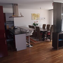Eine moderne Wohnung mit Holzfußboden und einer offenen Koch- und Essbereich. Der Tisch ist mit stilvollen Stühlen umgeben, und es gibt einen Fernseher im Wohnzimmer.