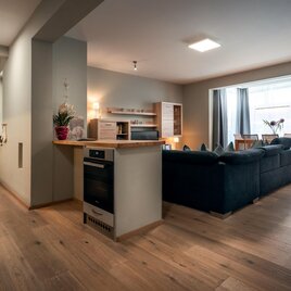 Eine moderne Wohnung mit offener Küche und Wohnzimmer. Der Raum ist hell und freundlich mit Holzfußboden und großen Fenstern.