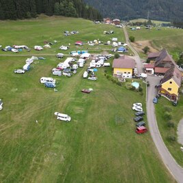 Ein Campingplatz mit vielen Wohnmobilen und Zelten in einer grünen Landschaft. Im Hintergrund sind Gebäude und Bäume zu sehen. | © Camping TÜRKIS - Mayer-Baumessner