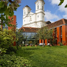 Ein schöner Garten mit grüner Wiese und bunten Pflanzen. Im Hintergrund steht ein eindrucksvolles, historisches Gebäude mit Türmen. | © Der Ederer