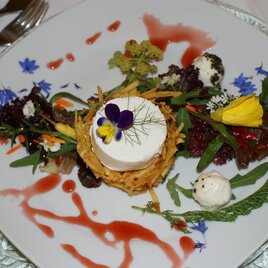 Ein kunstvoll angerichteter Teller mit frischem Salat und essbaren Blumen. In der Mitte befindet sich eine cremige Speise, umgeben von bunten Garnierungen. | © Herbert Wölkart