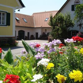 Ein schöner Innenhof mit bunten Blumen und gepflegten Pflanzen. Im Hintergrund sind charmante, traditionelle Gebäude zu sehen. | © Erlebnis- und Genusswelt Farmer-Rabensteiner