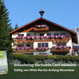 A charming house with colorful flower boxes in front of an impressive mountain landscape. The inscription provides information about the Schladming-Dachstein Card and its validity.