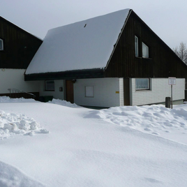 A large, snow-covered property with a two-story house. The sky is gray and overcast. | © Ursula Haller