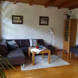 Ein gemütliches Wohnzimmer mit einer dunklen Couch und einem Holztisch. Helle Wände und große Fenster sorgen für eine freundliche Atmosphäre. | © Ferienhaus an der Traun, Bad Aussee