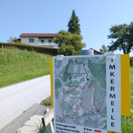 Ein Wegweiser zeigt zwei Wanderwege: Die Habeggrunde mit 8 km und die Ödgrabenerunde mit 5 km. Im Hintergrund sieht man ein Haus und einen klaren blauen Himmel. | © MR