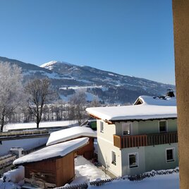A snowy landscape with a cozy house. In the background, snow-covered mountains and a blue sky can be seen.