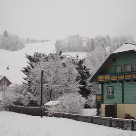 A snowy village with traditional houses. In the background, there are snow-covered hills and a cable car.