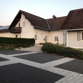 Ein modernes Haus mit einem schrägen Dach und einem Balkonen. Der Außenbereich ist ordentlich mit einem gepflasterten Weg und grünen Sträuchern gestaltet. | © Ferienwohnung Peklar | Karlheinz Peklar