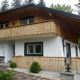 Ein gemütliches Holzhaus mit einem Balkon und einem einladenden Eingangsbereich. Es ist umgeben von Bäumen und einer gepflegten Landschaft. | © Vroni Rastl